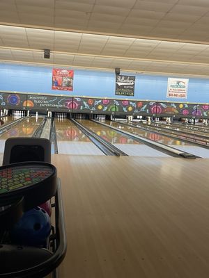 A vertical view of empty bowling lanes with a blue bowling ball in a rack in the foreground.