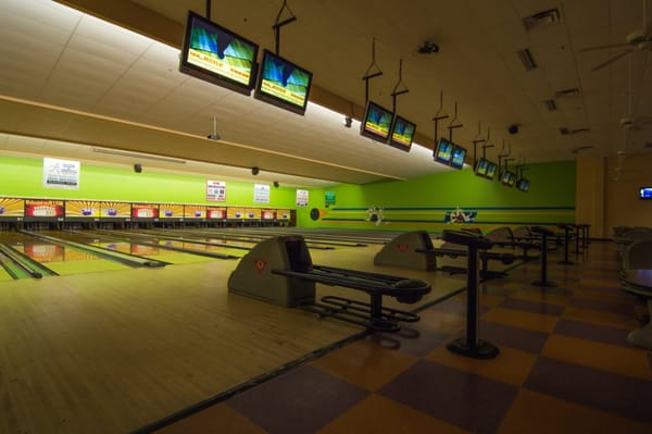 Interior view of empty bowling lanes with overhead monitors and lime green walls.
