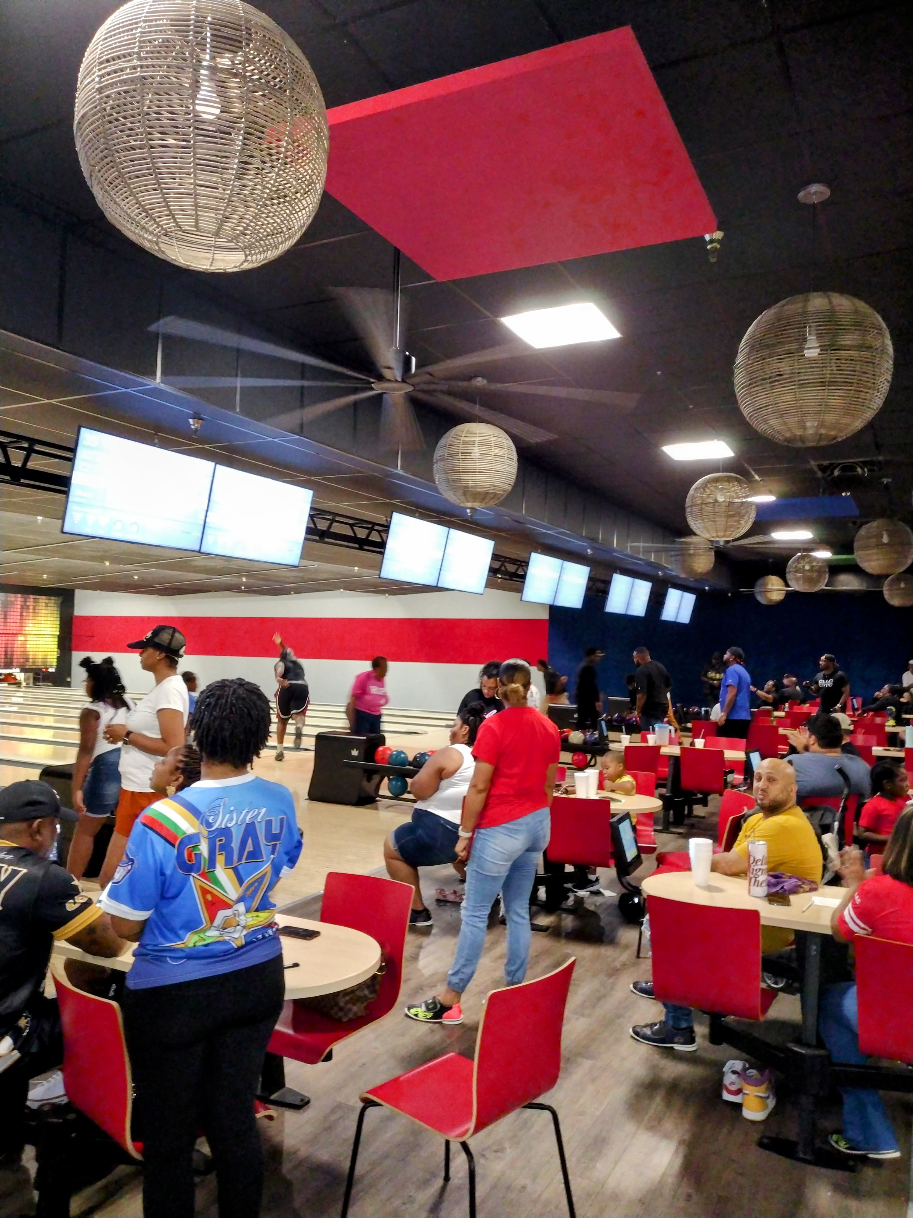A bustling bowling center interior with people socialising near lanes under modern decorative light fixtures.