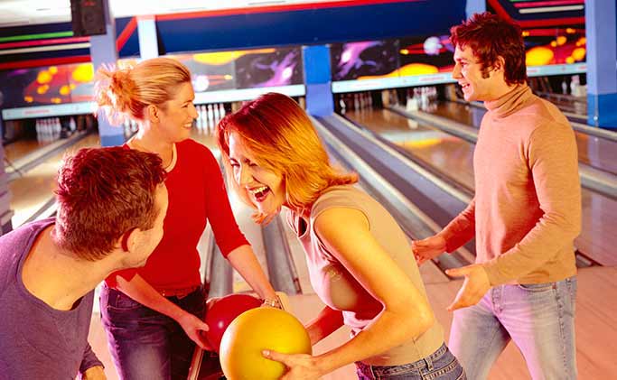 A group of friends laughing and holding bowling balls together at the bowling lanes.