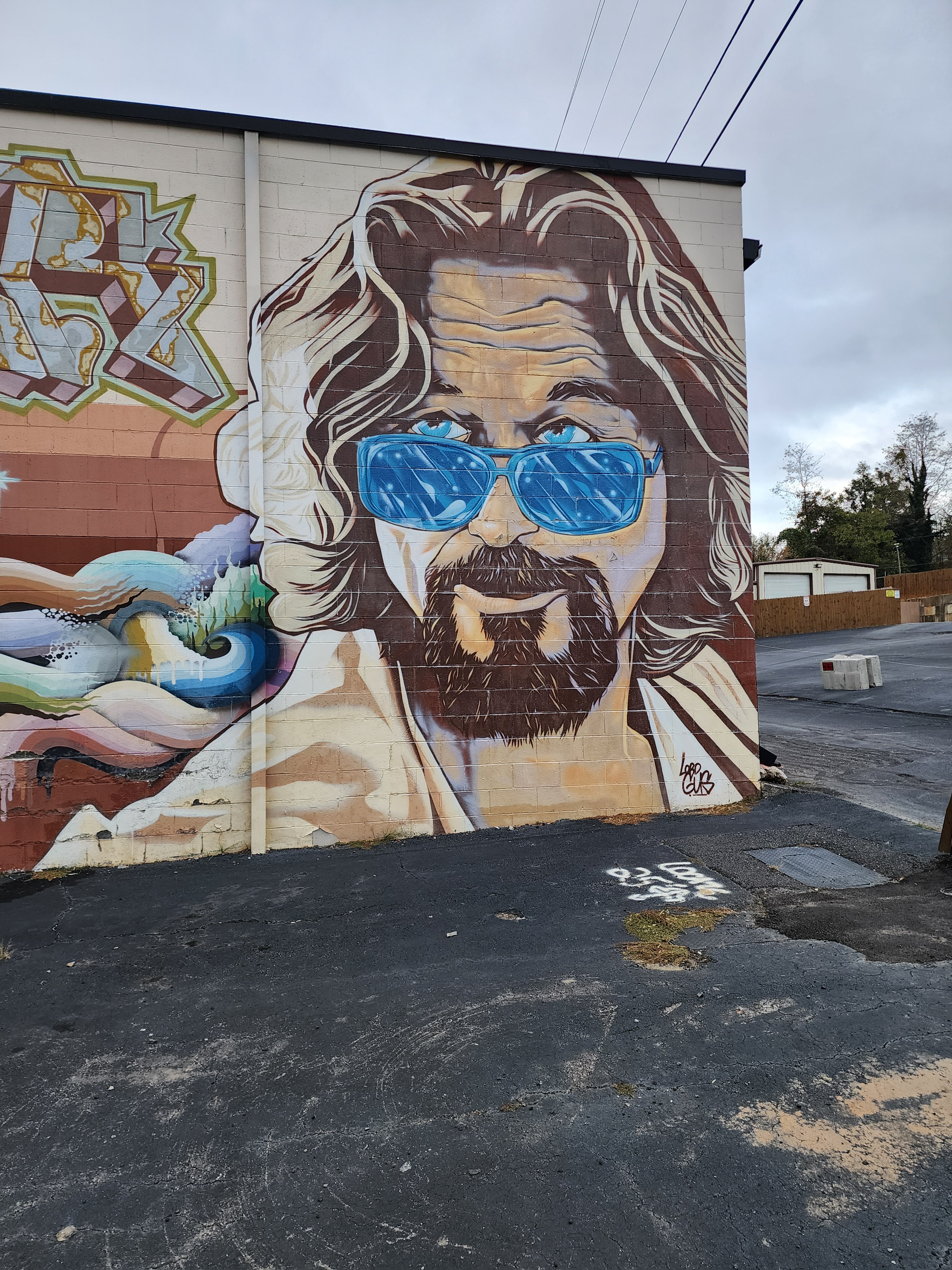 A large mural of a bearded man with blue sunglasses painted on an exterior cinder block wall.