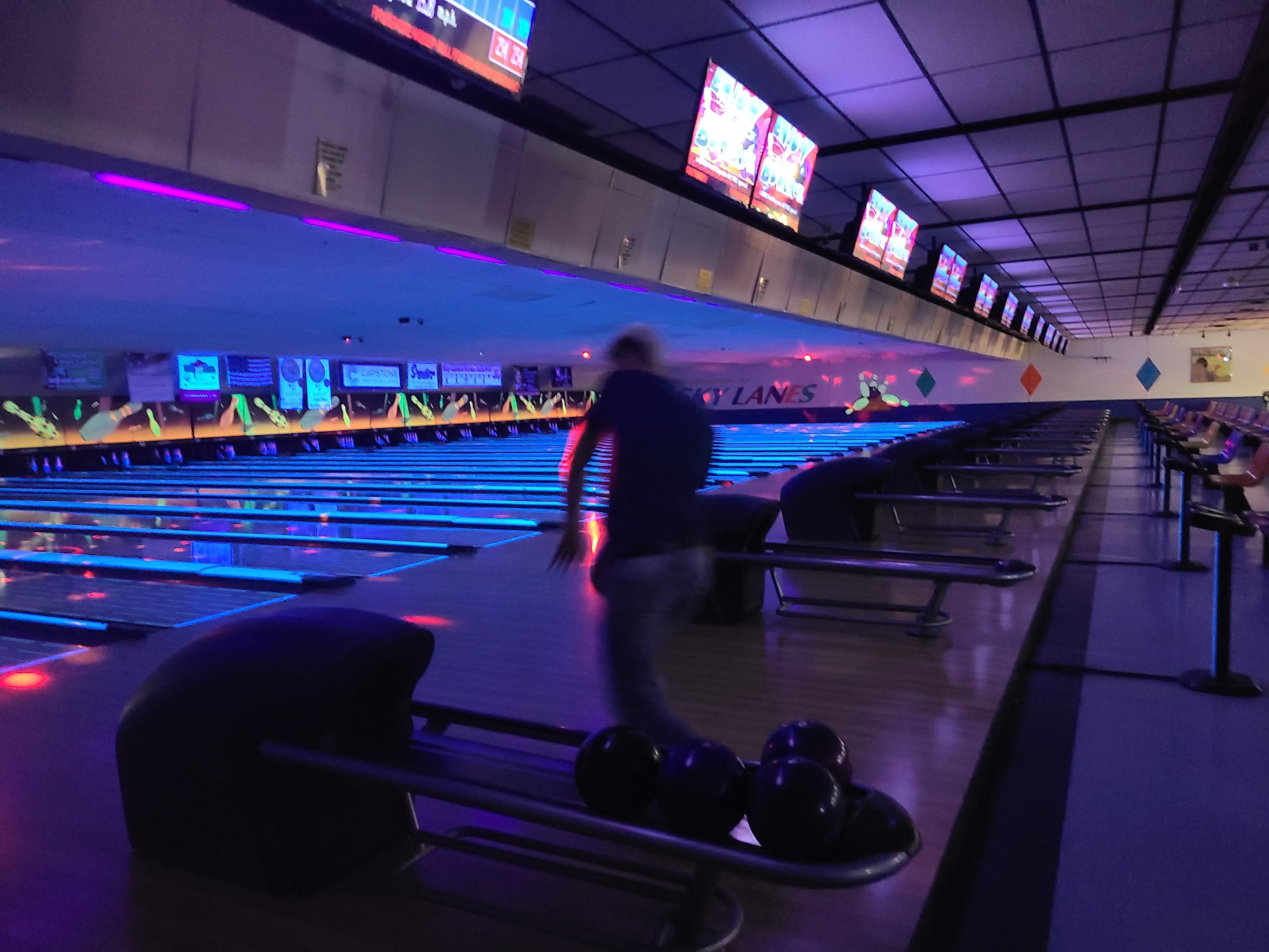 A person bowls under vibrant blue and purple neon lights at Sky Lanes.