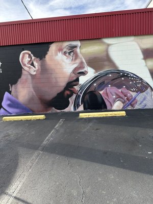 A large mural on an exterior cinderblock wall depicts a man in a purple shirt next to a bowling ball.