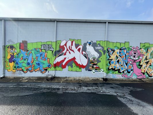 A long white exterior wall featuring a vibrant multi-colored graffiti mural with cartoon characters and street art.