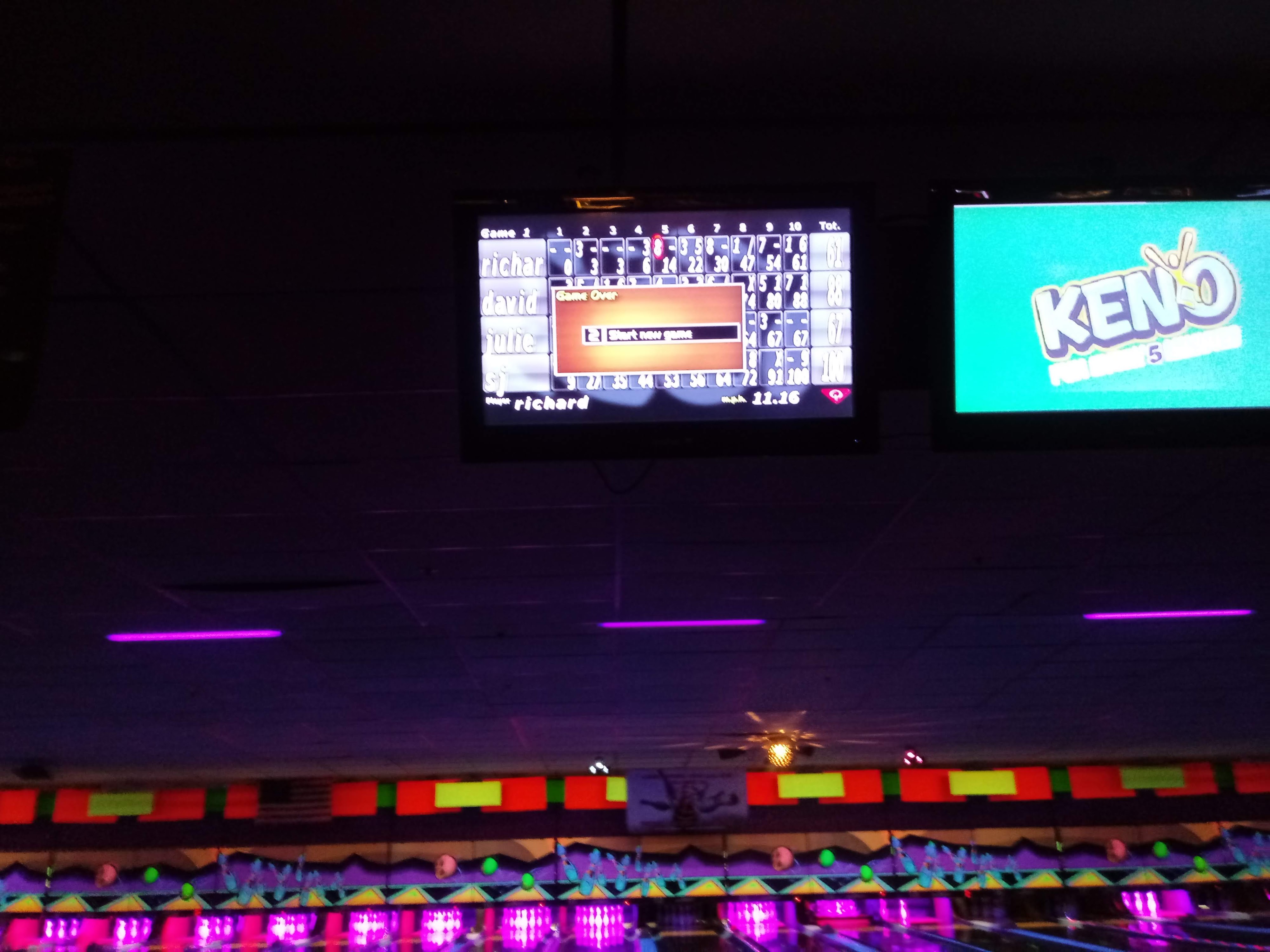 An overhead bowling scoring monitor displays game results under neon pink and green cosmic lighting.
