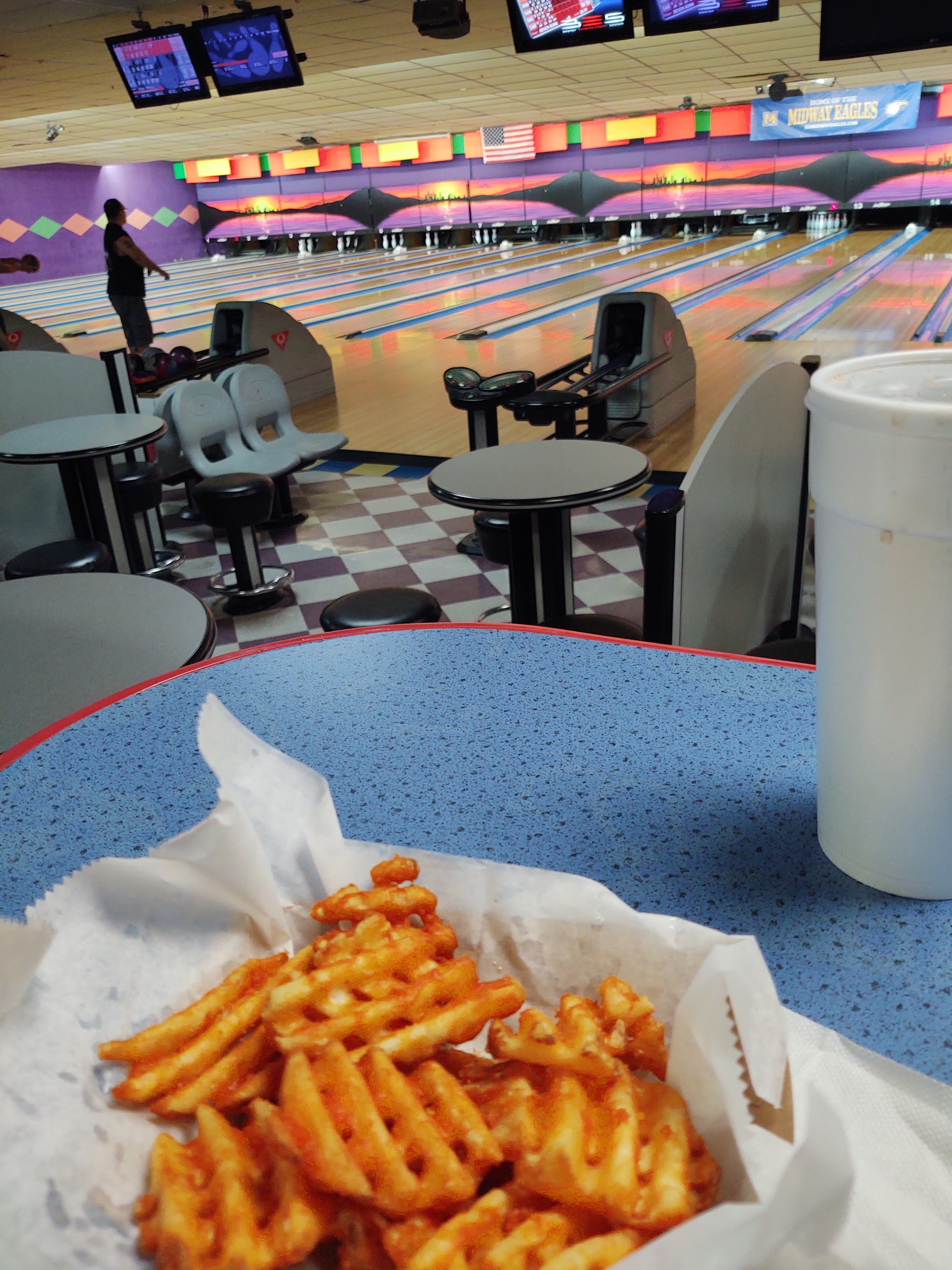 A basket of waffle fries and a drink on a blue table overlooking bowling lanes at Capital Bowl.