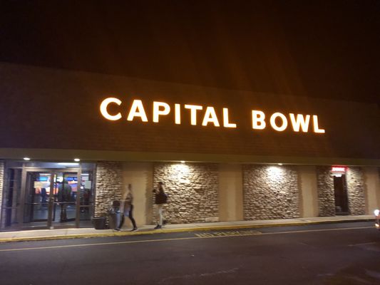 Nighttime exterior view of Capital Bowl with glowing orange sign above the entrance and stone walls.