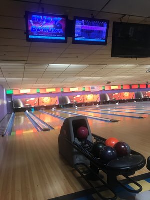 A view down several bowling lanes with a ball return and colorful bowling balls in the foreground.