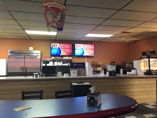 A snack bar counter with digital menus, a soda fountain, and a hanging soft pretzel sign in a bowling center.