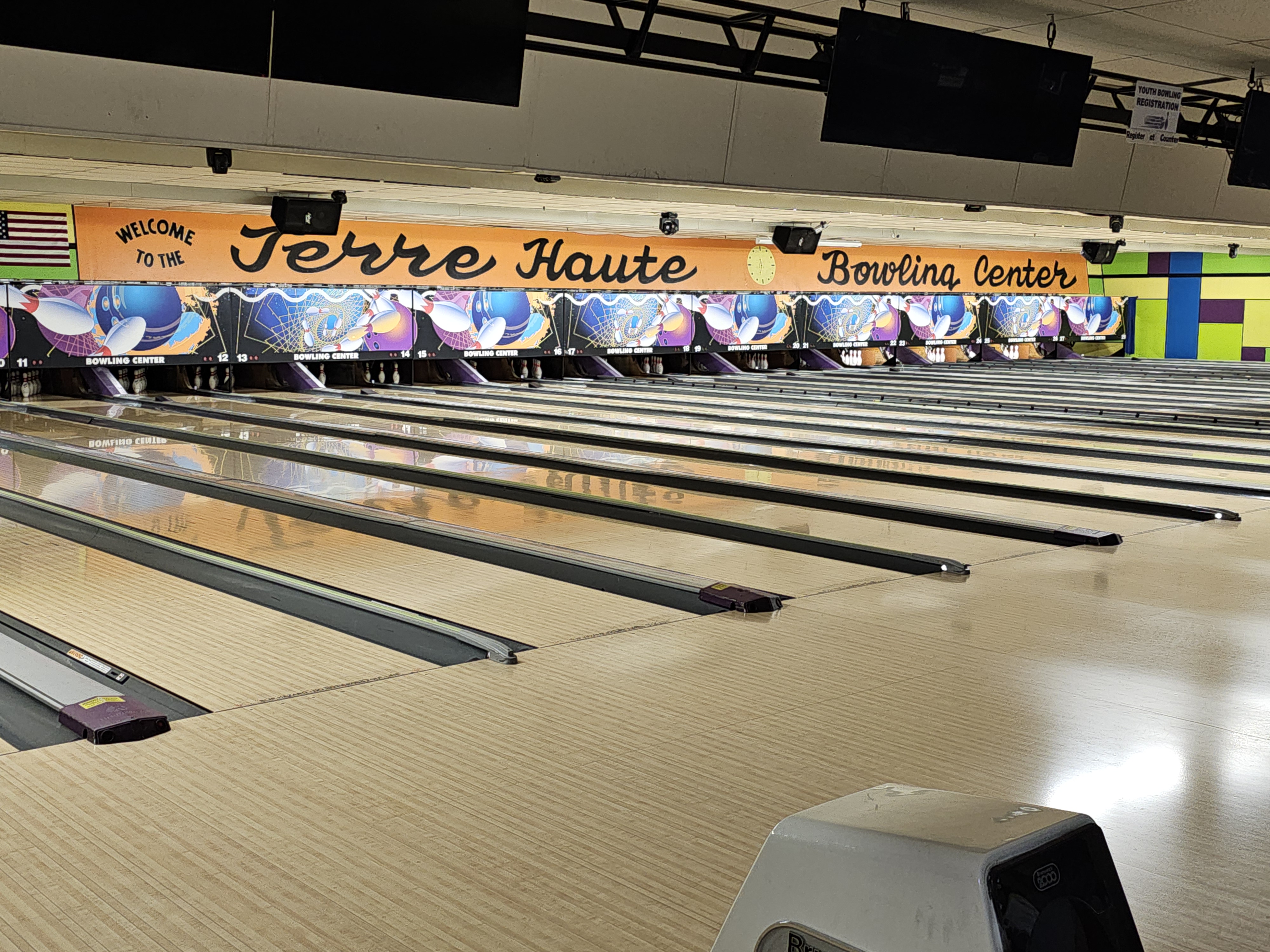 A wide view of polished wooden bowling lanes under a large orange banner for Terre Haute Bowling Center.