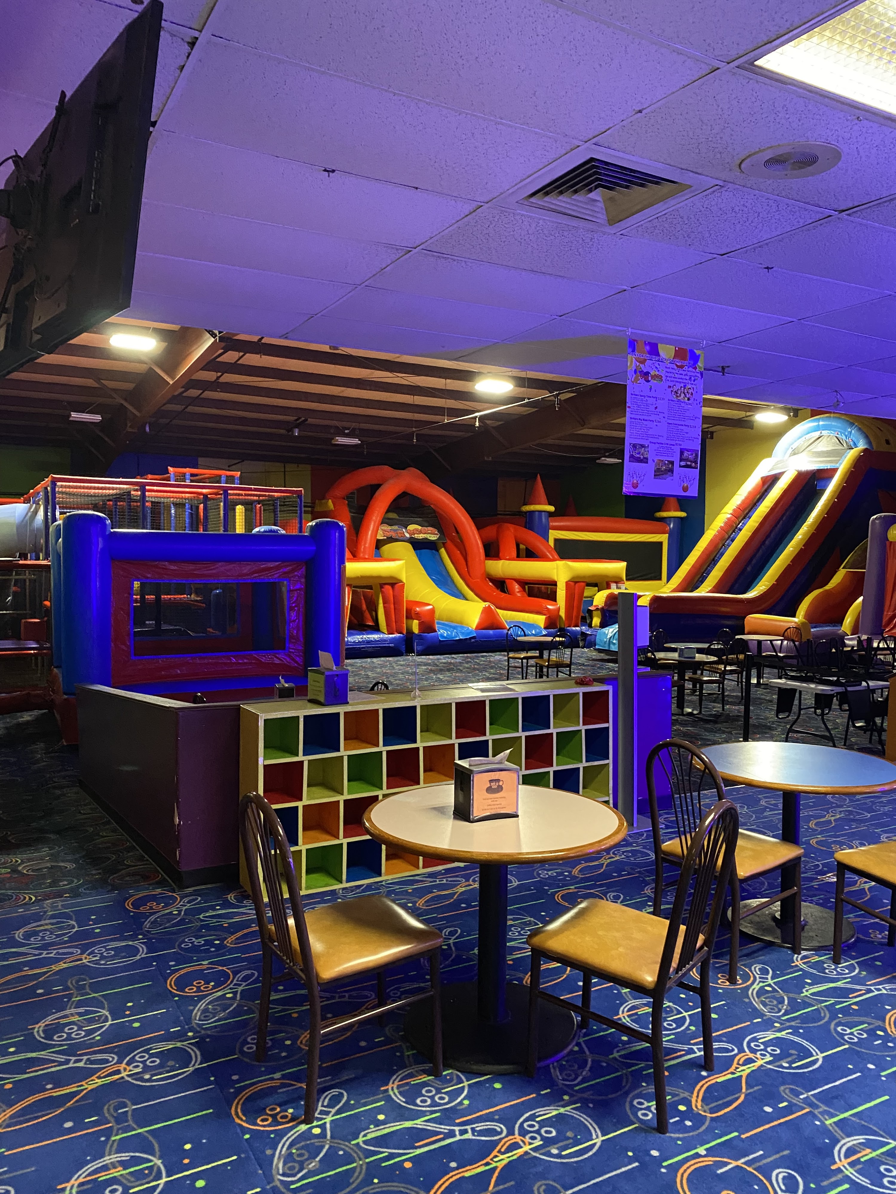 A colorful indoor soft play area with inflatable slides and obstacle courses behind cafe tables and chairs.