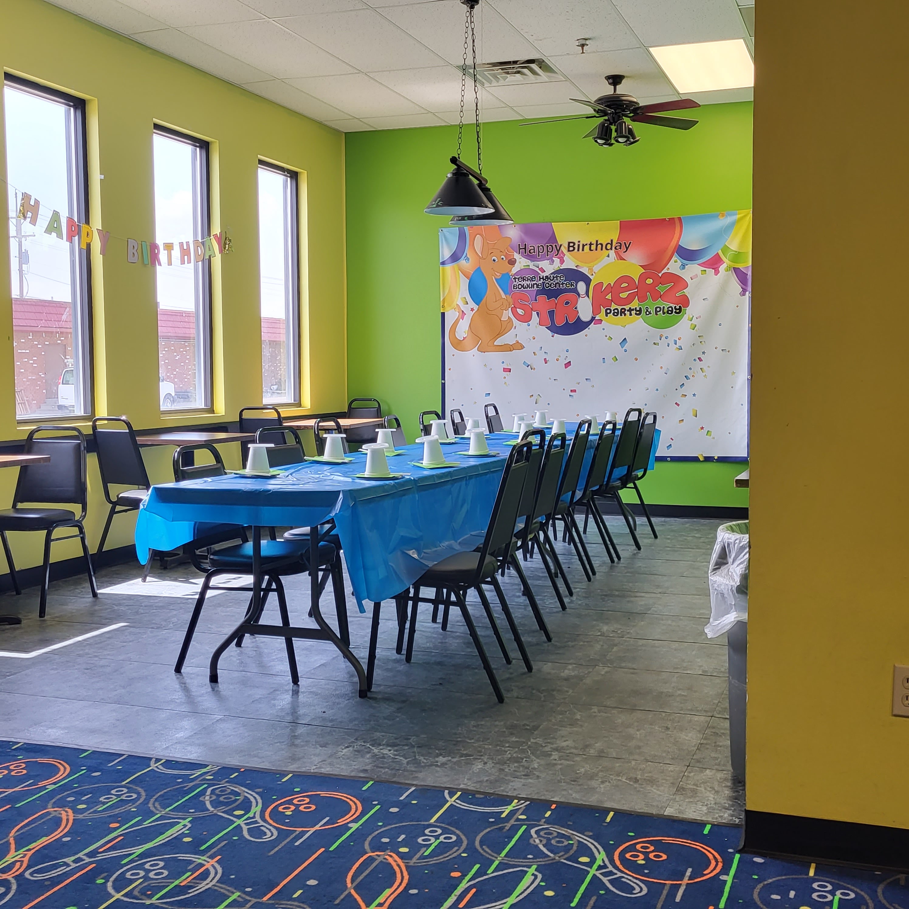 A festive birthday party room with a long table, blue tablecloth, and a Strikers Party and Play banner.
