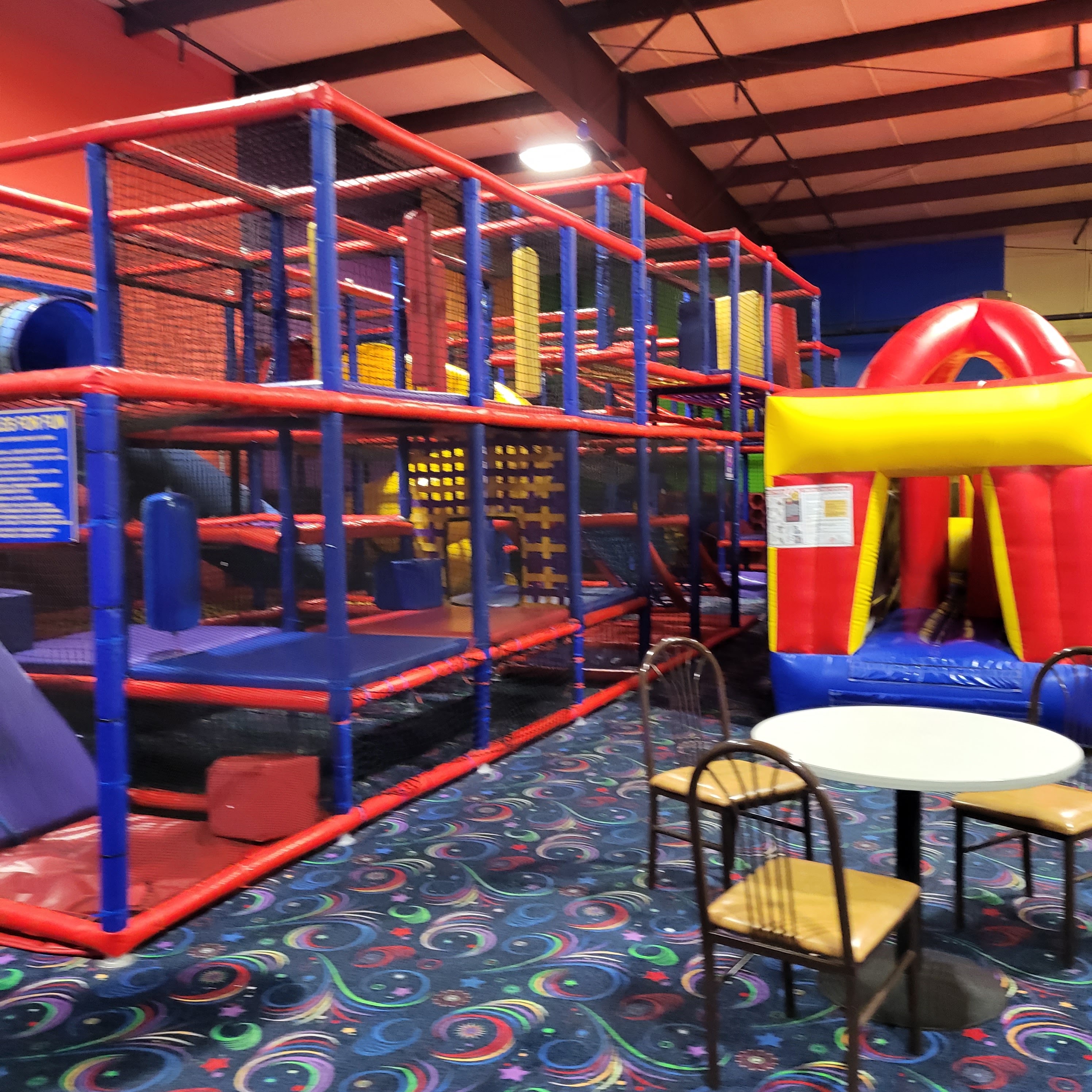 A large multi-level indoor soft play playground and red inflatable bounce house next to a cafe table and chairs.