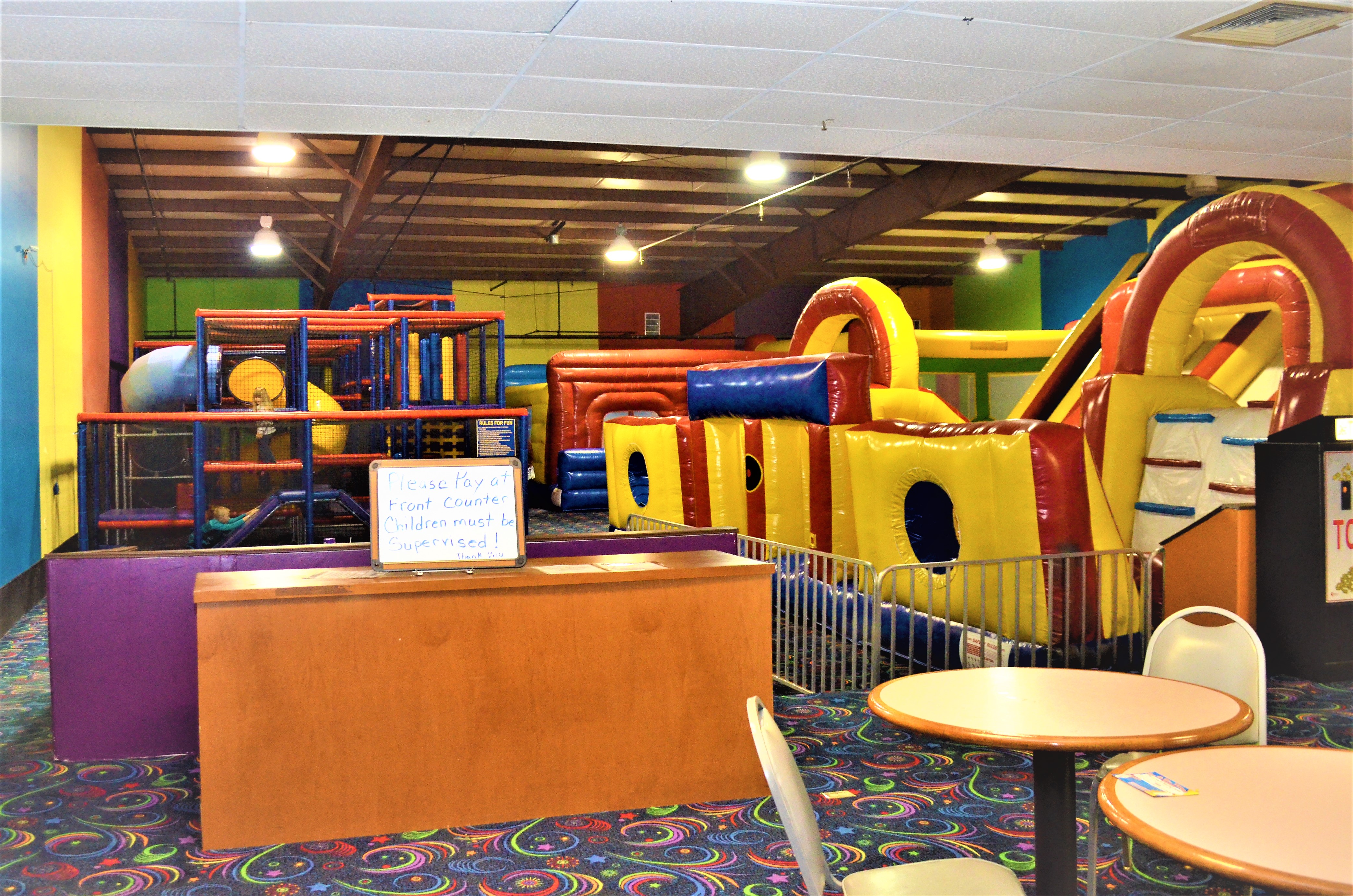 A bright indoor playground with colorful inflatable slides and a large soft-play climbing structure.