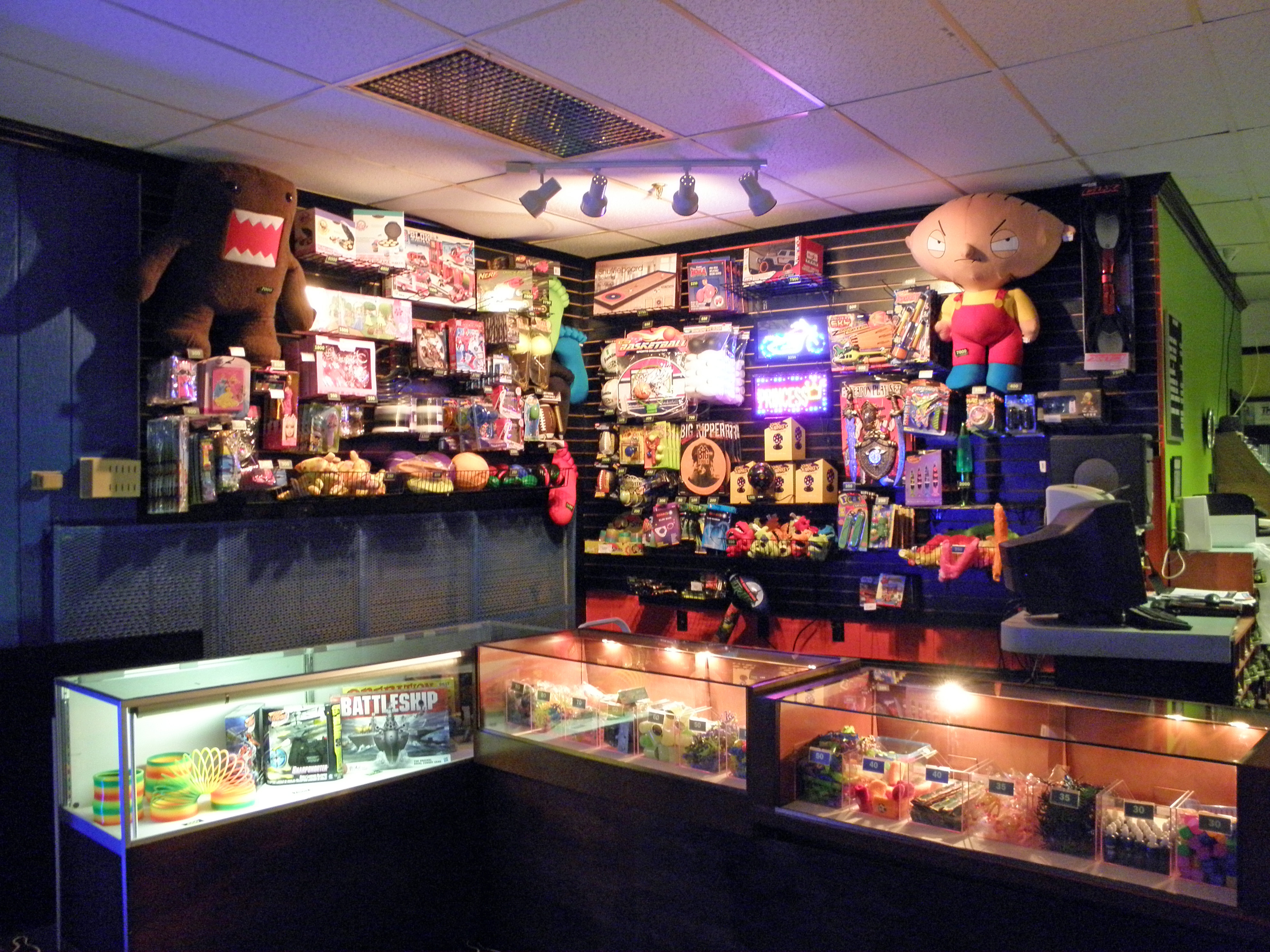 A colorful arcade redemption counter filled with plush toys, board games, and prizes in glass display cases.