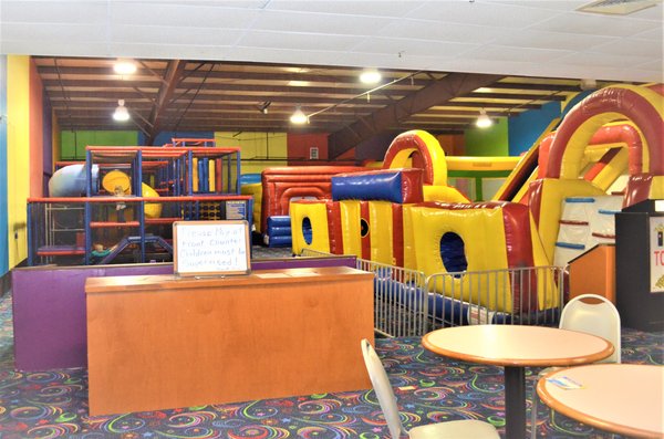An indoor playground with large colorful inflatables and a multi-level soft play climbing structure.