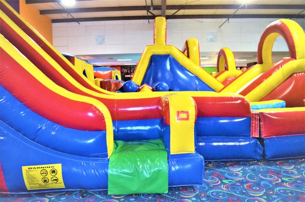 A large and colorful inflatable playground with slides and tunnels inside a family entertainment center.