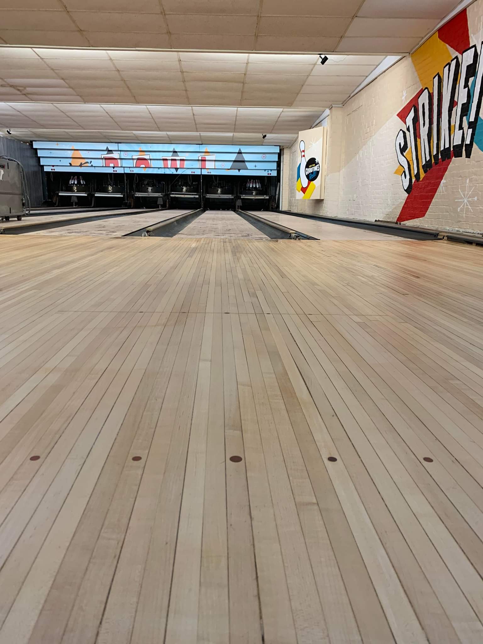 A bowling alley with multiple lanes, pin setters, and colorful murals on the right wall.