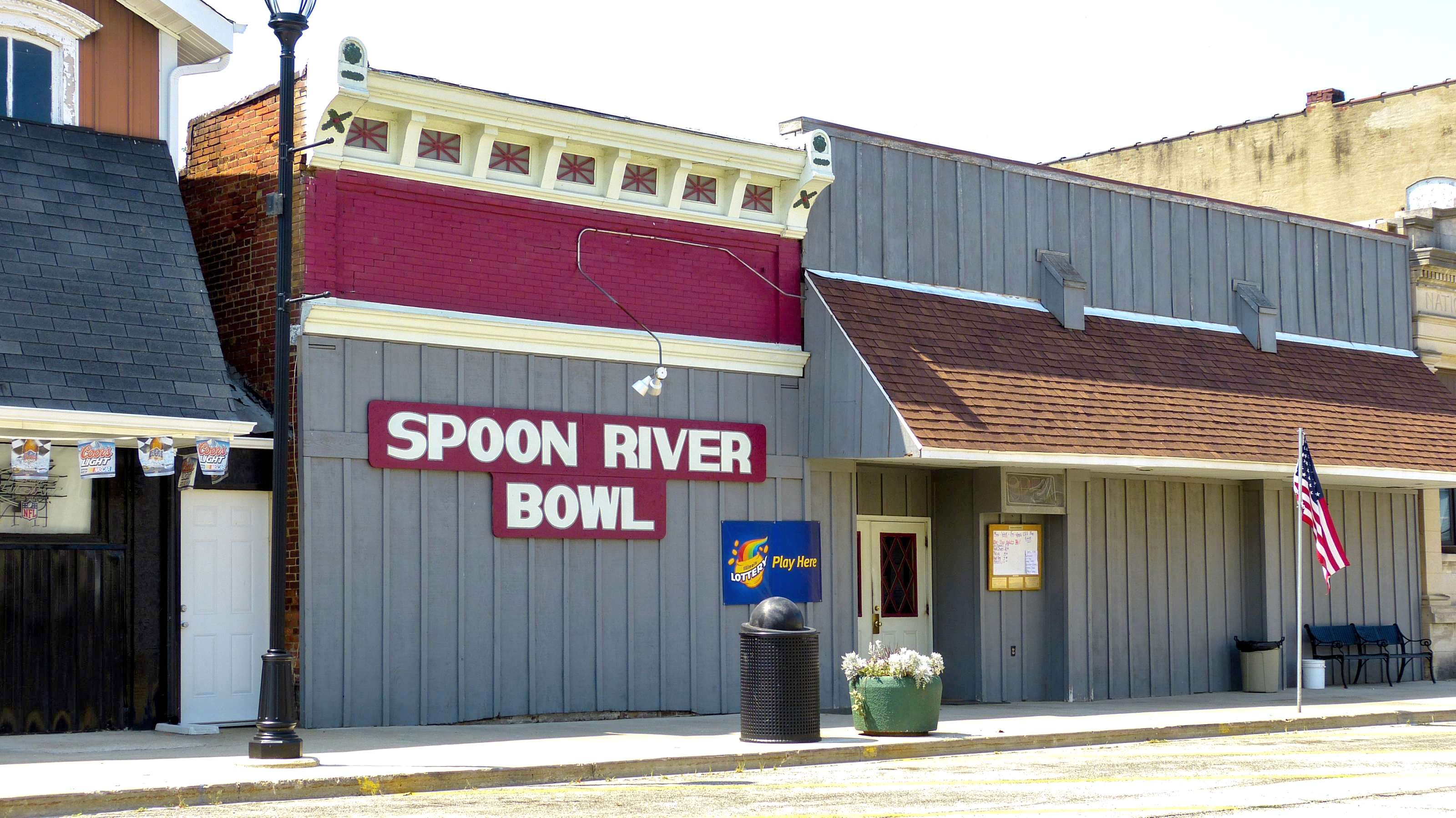 Exterior view of Spoon River Bowl, a building with a red and white sign, grey siding, and an American flag.