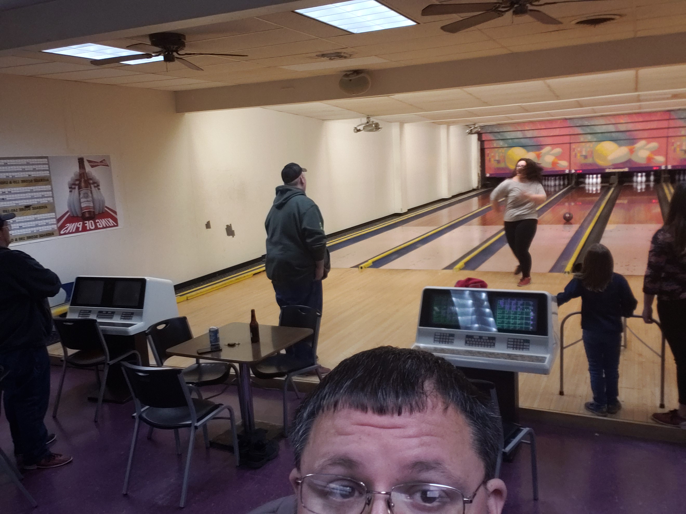 A group of people bowling on lanes with automatic scoring, a person in the foreground looking towards the action.