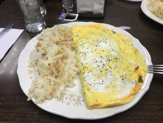 A breakfast plate with an omelette and hash browns on a table.