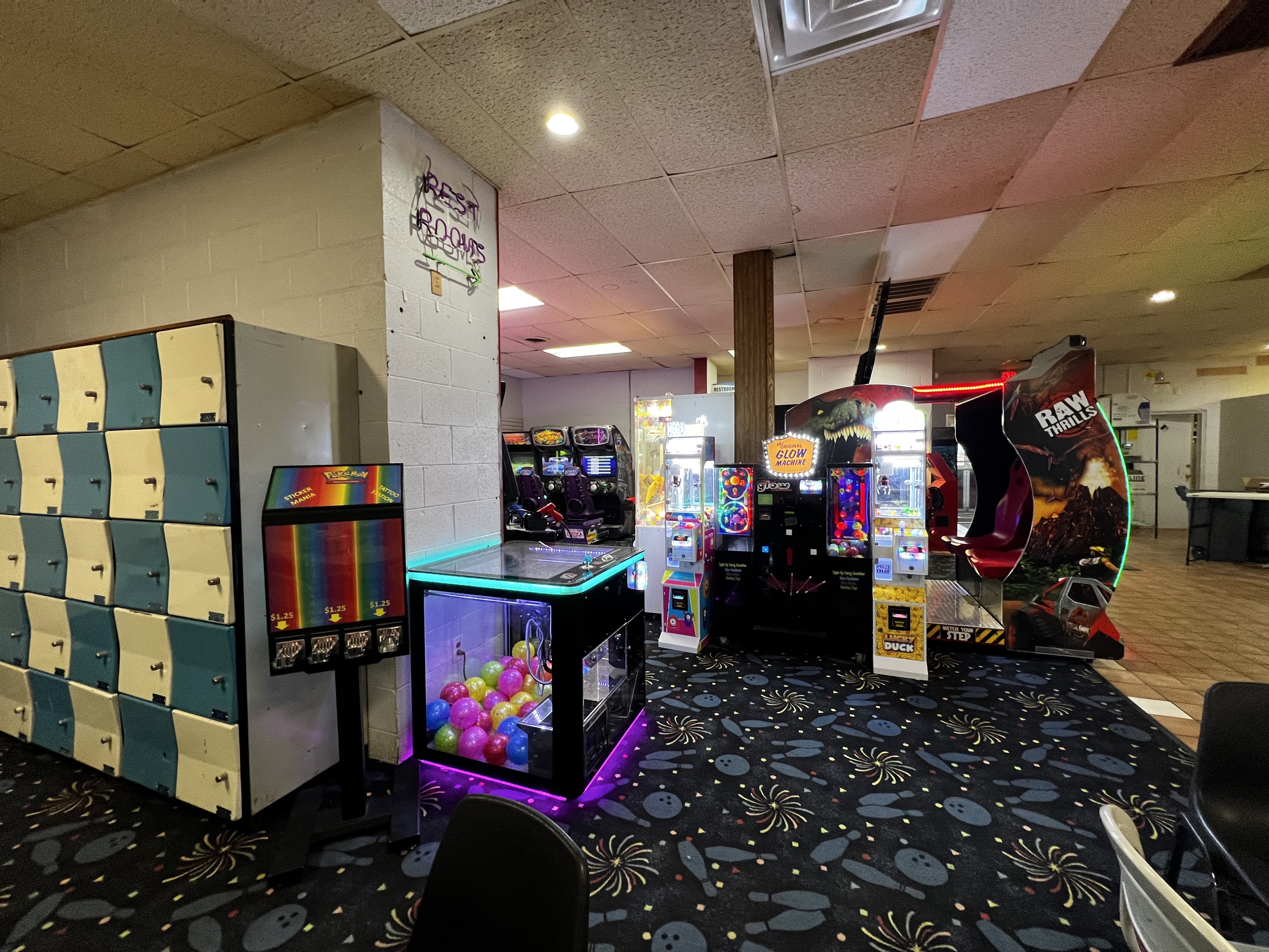 An arcade area in a bowling alley with game machines, blue and white lockers, and bowling-themed carpet.