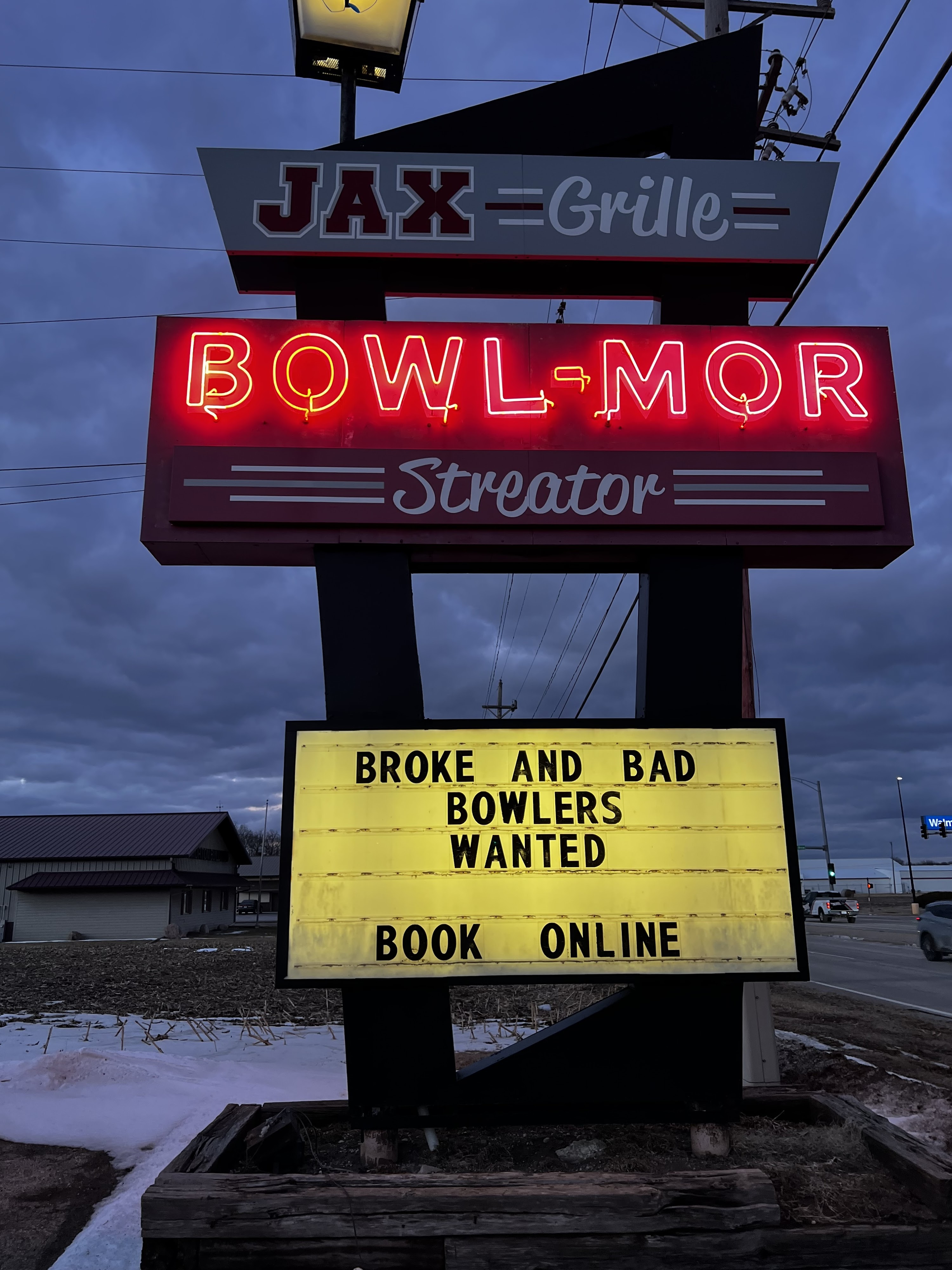 A roadside sign for Bowl-Mor Streator and Jax Grille at dusk with a marquee reading Broke and Bad Bowlers Wanted.
