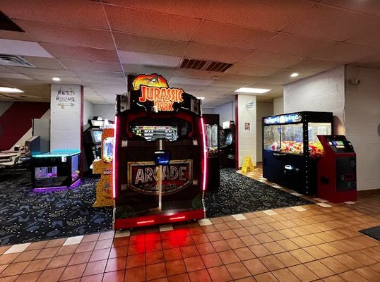 A bowling center arcade featuring a Jurassic Park game, a claw machine, and an air hockey table.