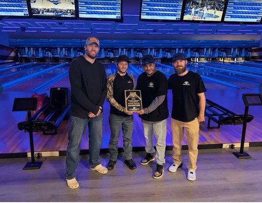 Four men standing on a bowling lane holding a championship plaque under blue lights.
