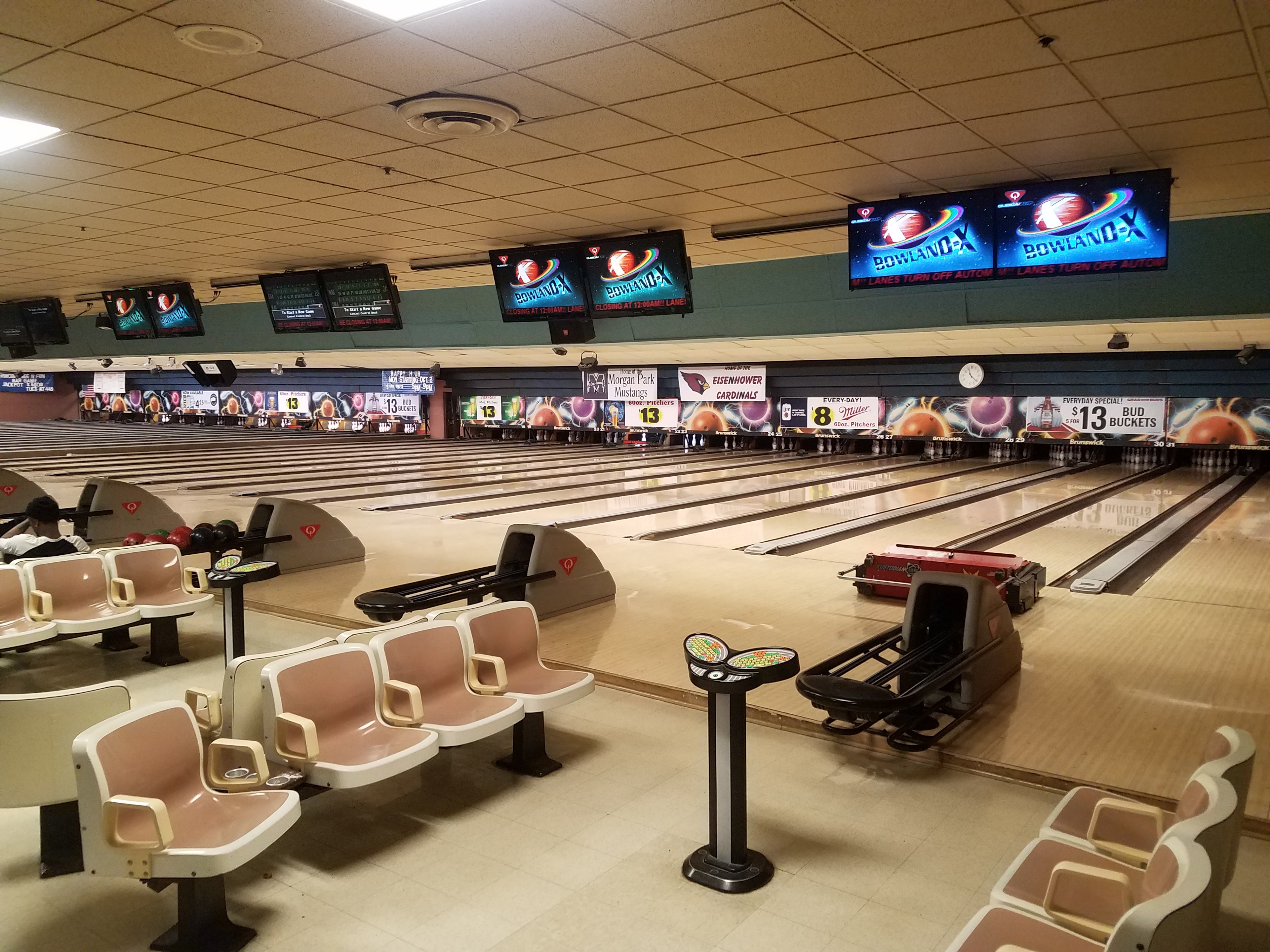 A wide view of several polished bowling lanes with tan plastic chairs and overhead scoring monitors.
