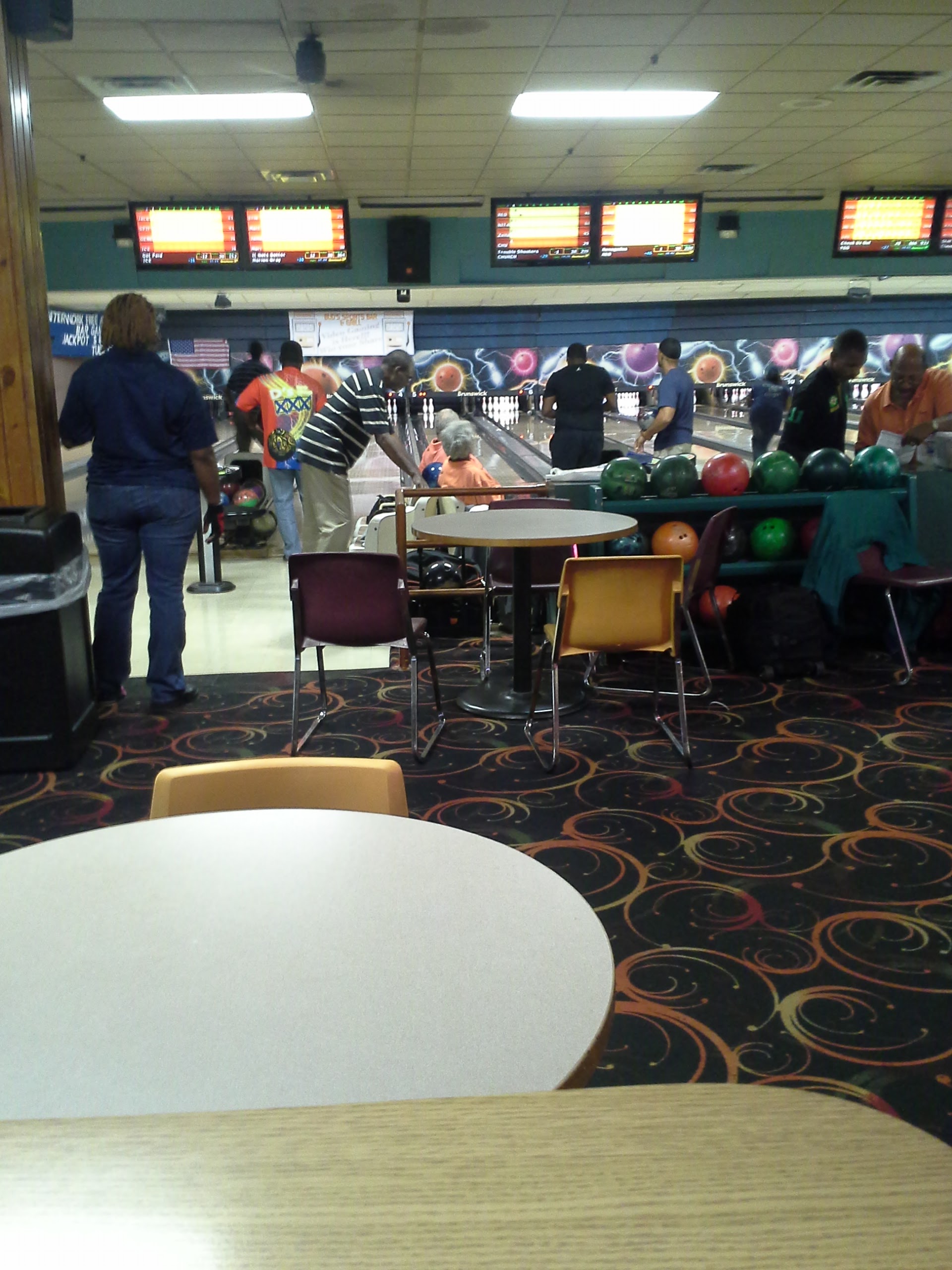 People bowling at an indoor alley with automatic scoring monitors and a seating area in the foreground.