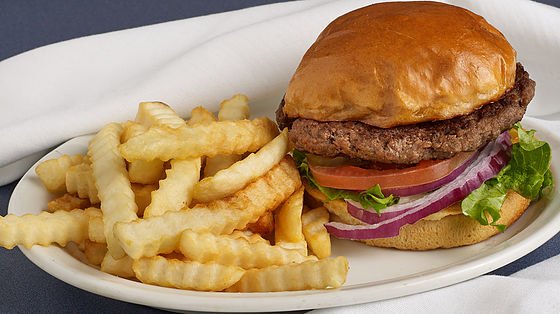 A hamburger with lettuce, tomato, and onion served with crinkle-cut fries on a white plate.