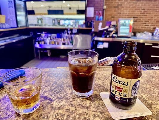 Three drinks including a beer bottle and two cocktails sitting on a bar counter.