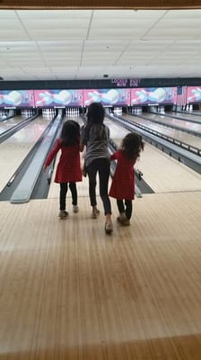 Three young girls walking toward bowling pins on a lane with bumper guards.