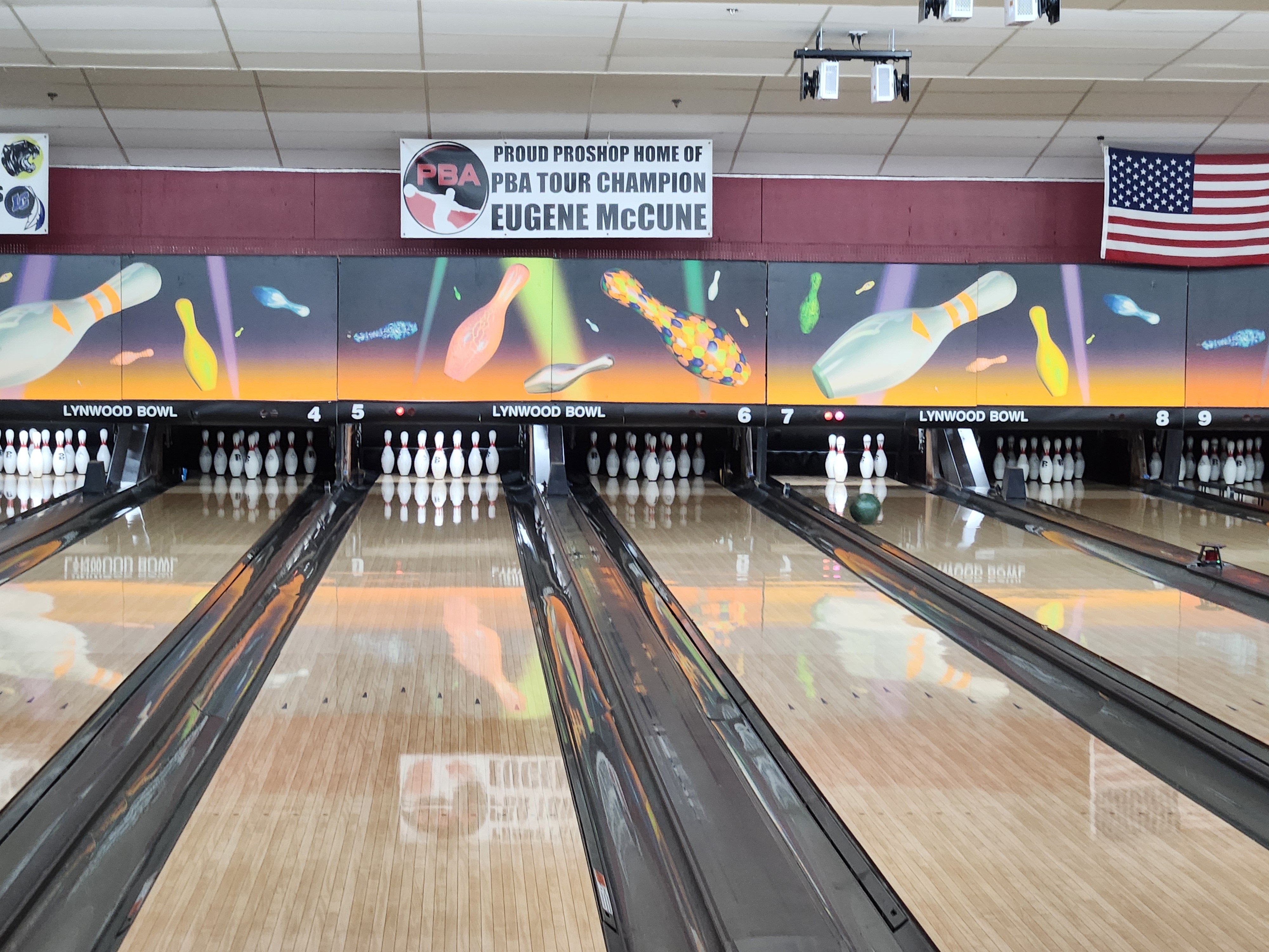 A straight-on view of polished bowling lanes with colorful pin graphics and a PBA Champion Eugene McCune banner.