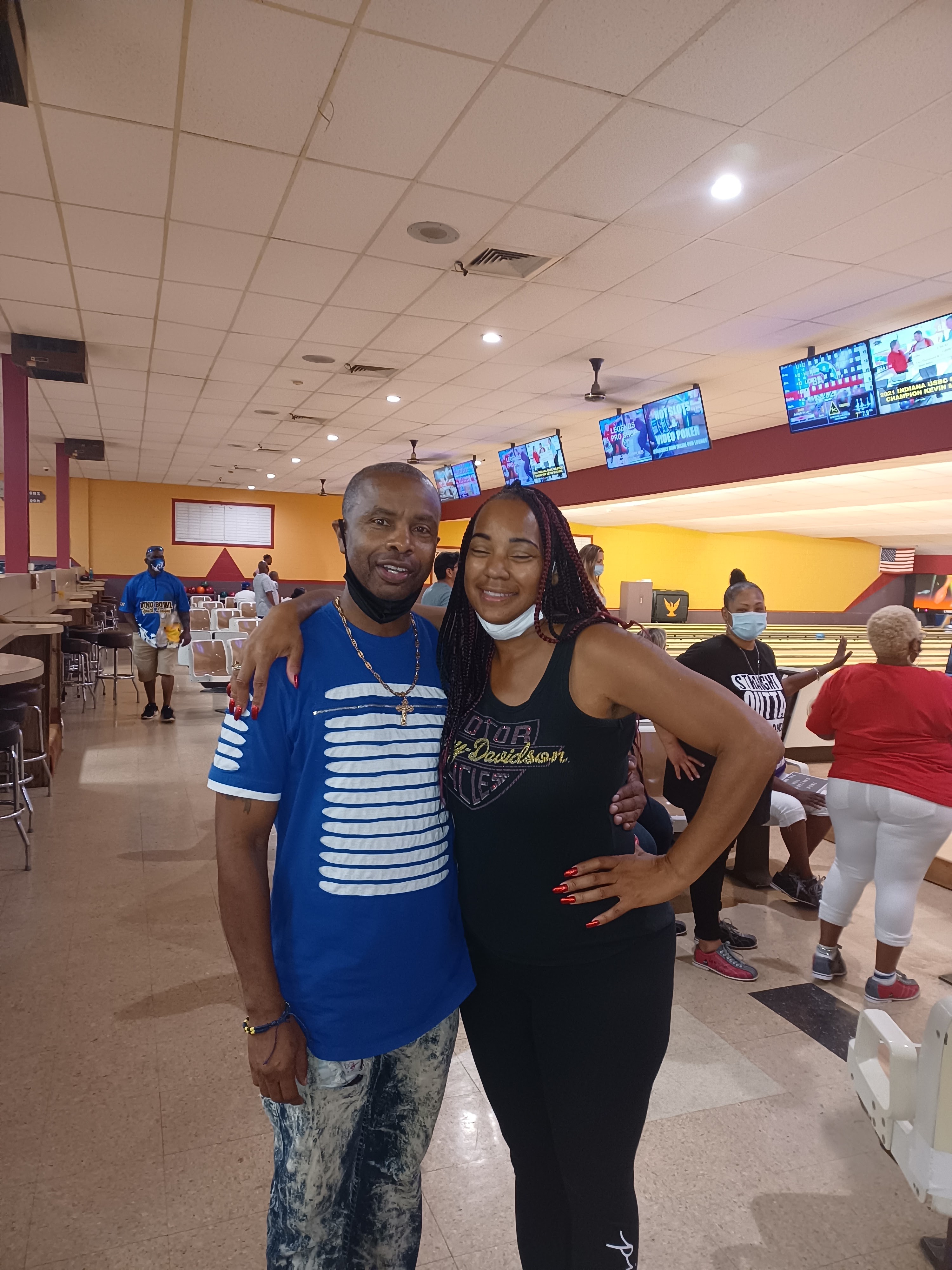 A man and woman pose together in a bowling center with lanes and scoring monitors in the background.
