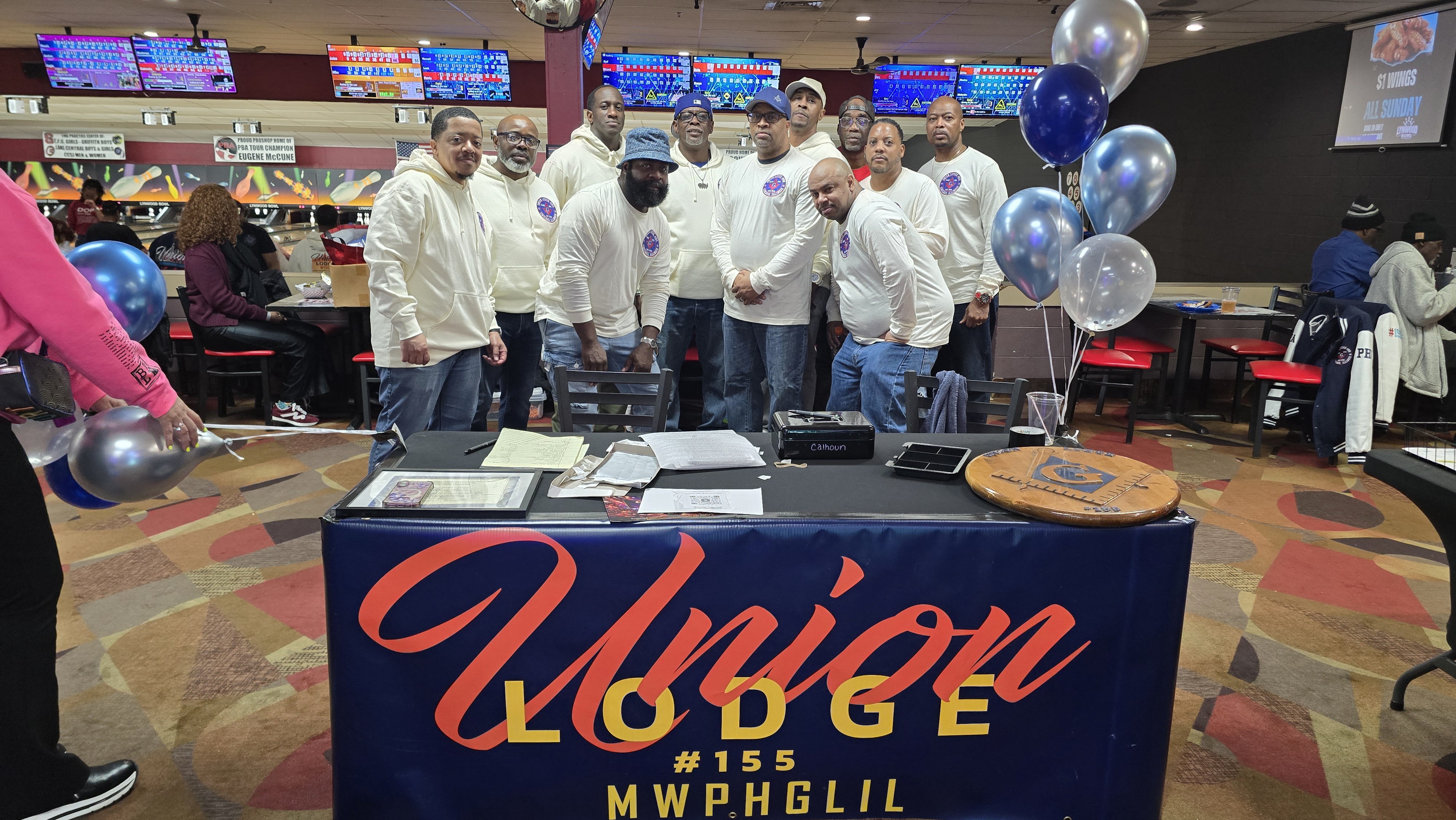 A group of men in matching cream-colored shirts posing behind a Union Lodge #155 banner at Lynwood Bowl.