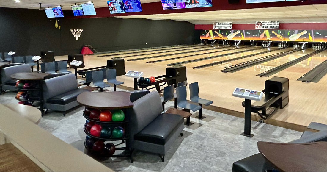 Wide view of bowling lanes with gray couch seating and automatic scoring monitors at Lynwood Bowl.