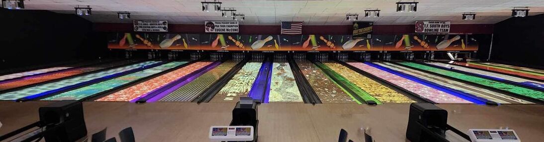 A wide view of bowling lanes at Lynwood Bowl featuring vibrant colorful digital projections on the lane surfaces.