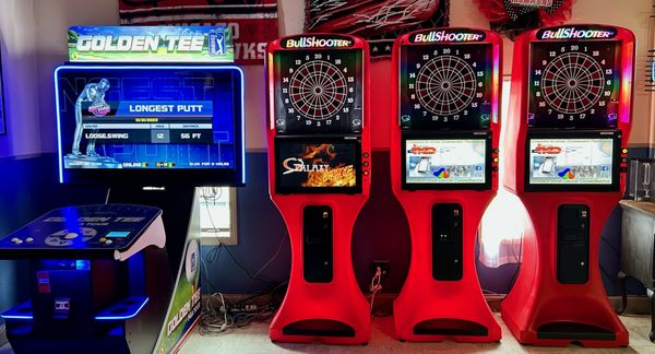 Four gaming cabinets including one Golden Tee golf machine and three red BullShooter dart boards.