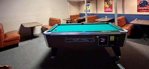 A green pool table in a lounge area with orange leather booths and Chicago sports team banners on the wall.