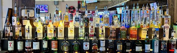 A wide, tiered display of various liquor bottles on black shelves at a bowling center bar.