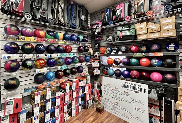 A bowling pro shop filled with rows of colorful bowling balls, bags, and a tournament bracket on a whiteboard.