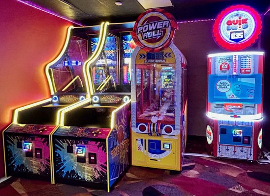 Three brightly lit arcade redemption games including Power Roll and Quik Drop stand against a wall.