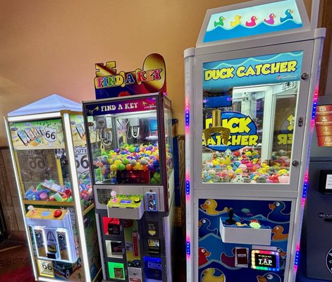 Three illuminated crane arcade machines including Duck Catcher and Find a Key filled with prizes.