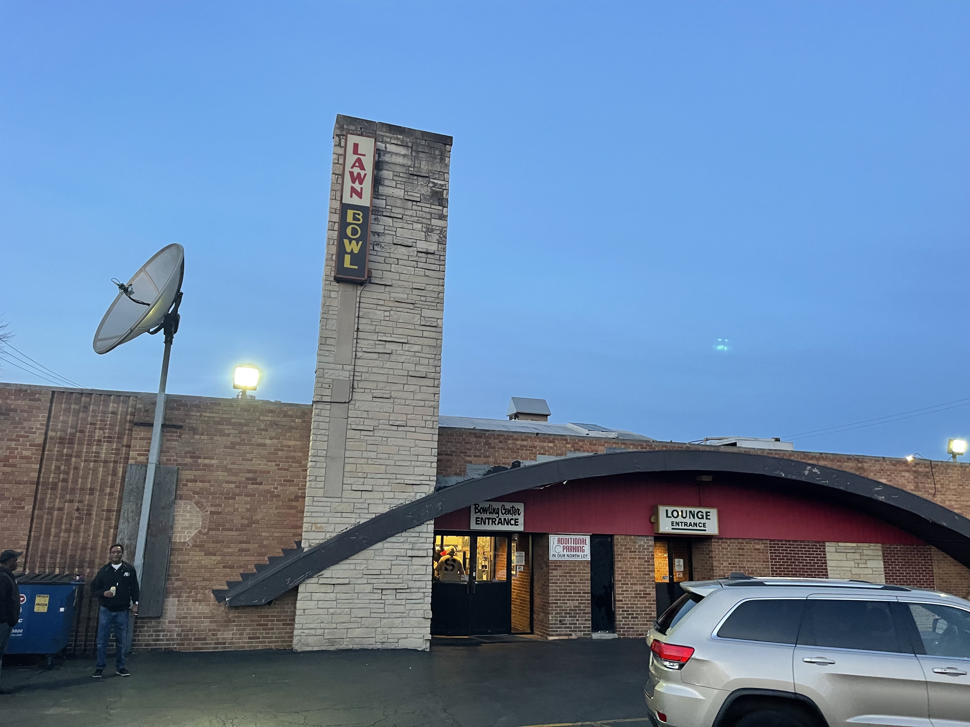 The brick exterior of Lawn Bowl featuring a tall stone sign pylon and arched entrances at dusk.