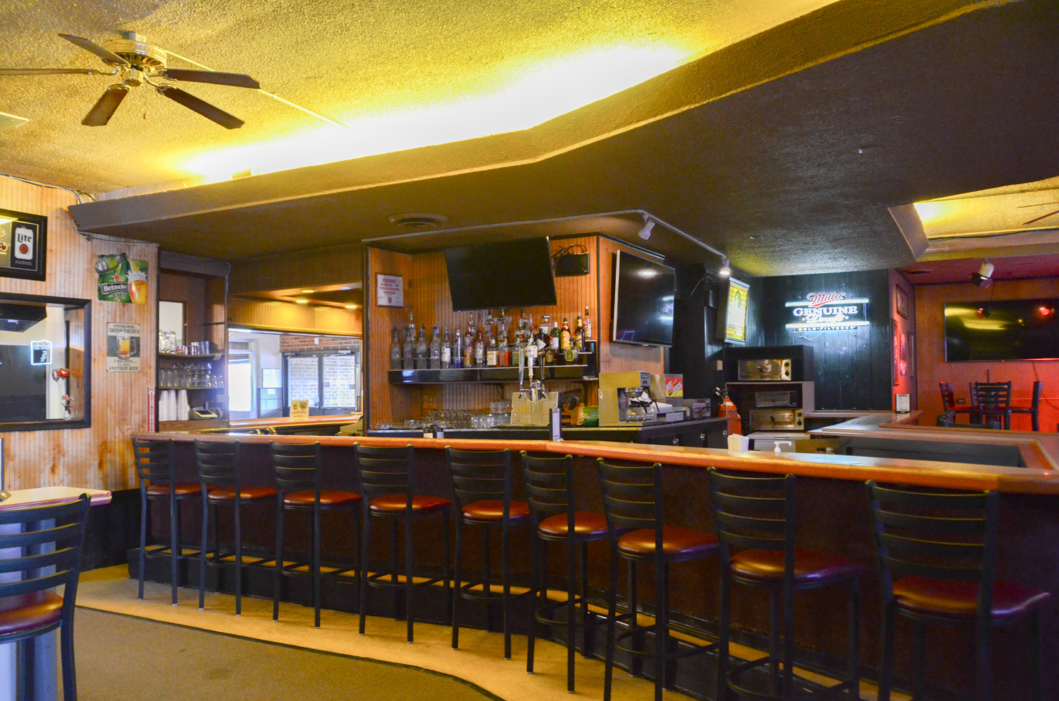 A long curved bar counter with several black and red stools inside a bowling center tavern area.