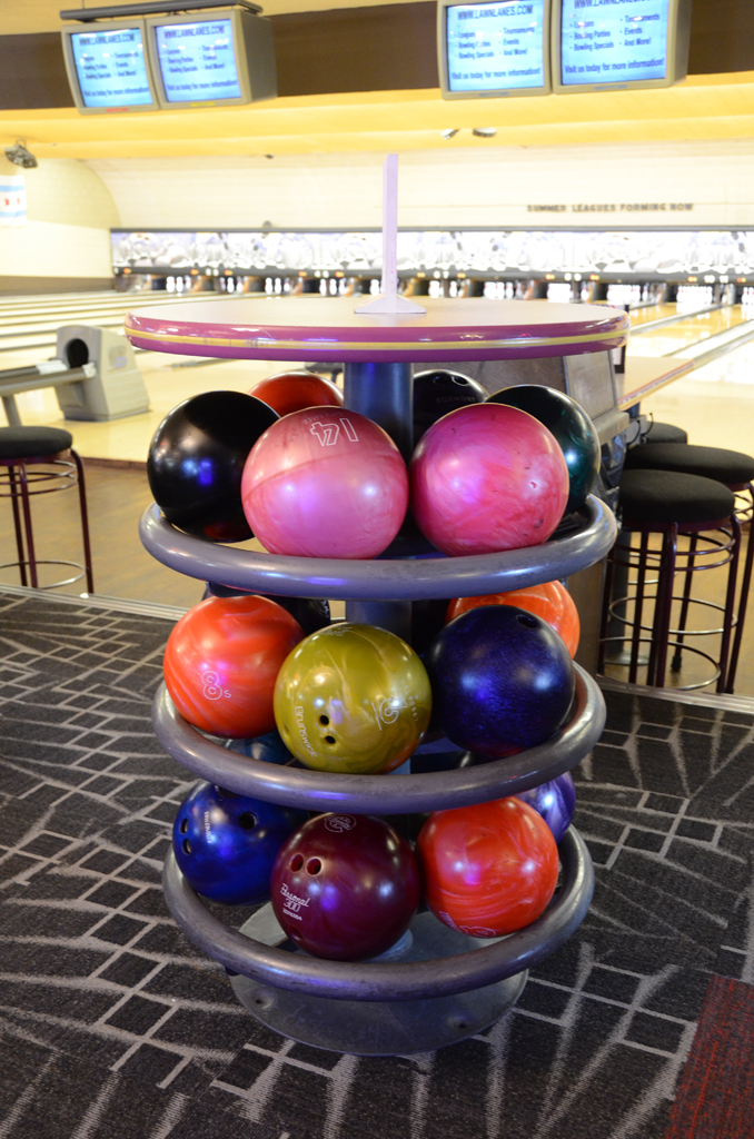 A circular three-tier bowling ball rack filled with colorful balls in a bowling alley.