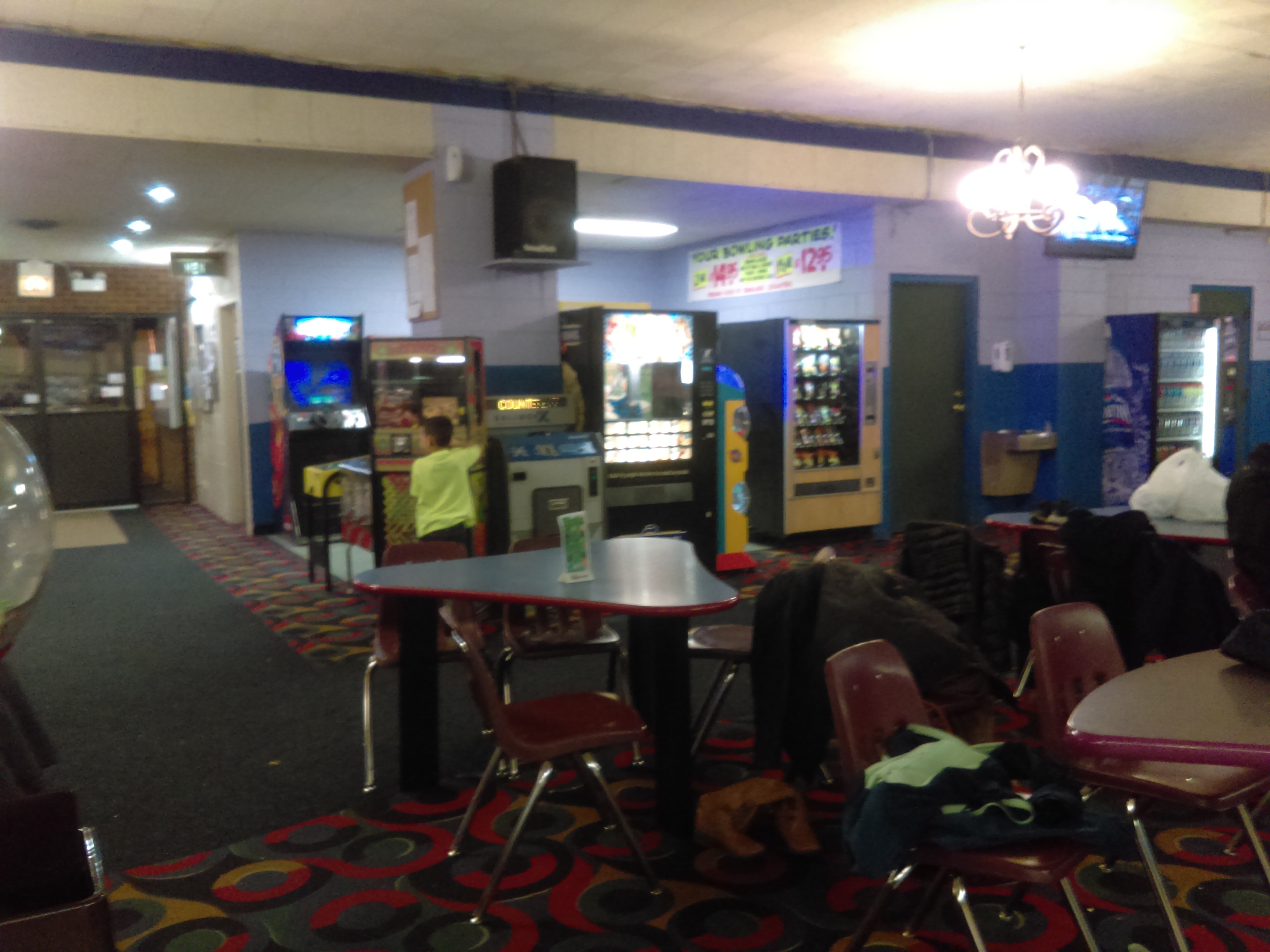 An arcade area with gaming machines, vending machines, and seating at triangular tables.