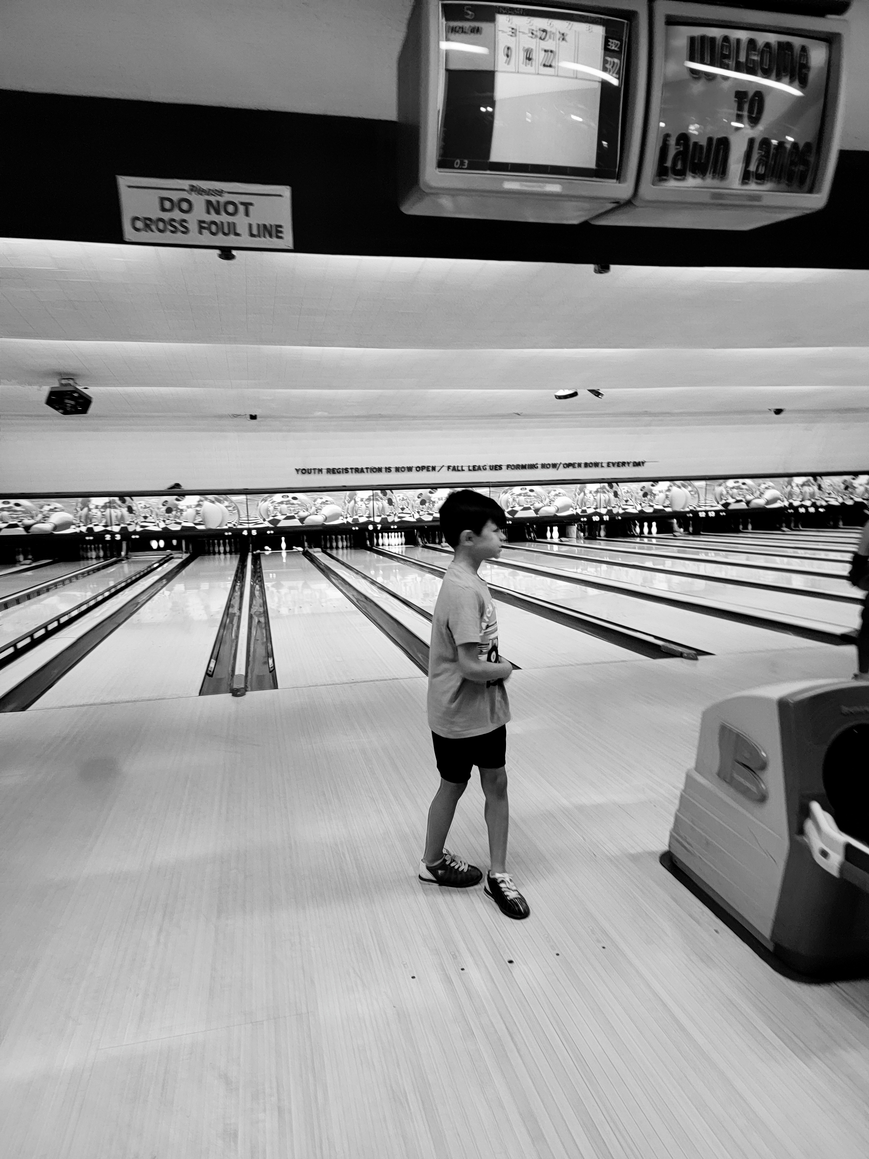 A boy stands on a bowling lane approach in this black and white photo at Lawn Lanes.